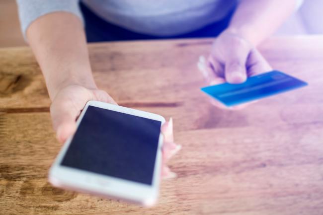 Une personne tenant une carte de crédit à la main tout en utilisant son téléphone portable.