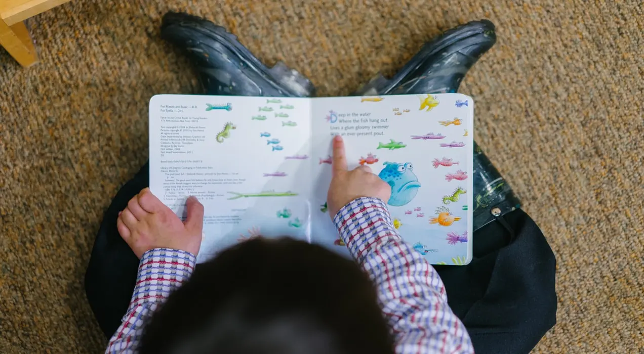 bambino sul pavimento che legge un libro sui pesci