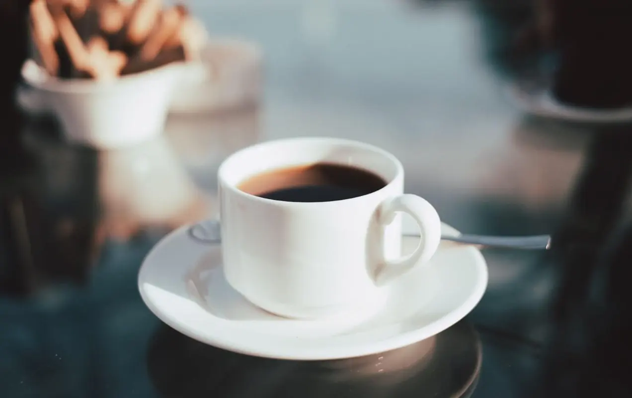 白い受け皿に座って、黒いコーヒーで満たされた短い白いコーヒーカップと反射ガラステーブル