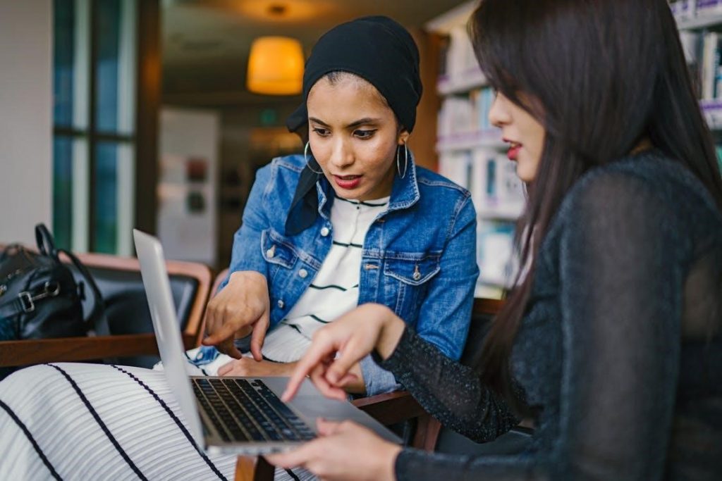 duas mulheres olhando e apontando para laptop macbook