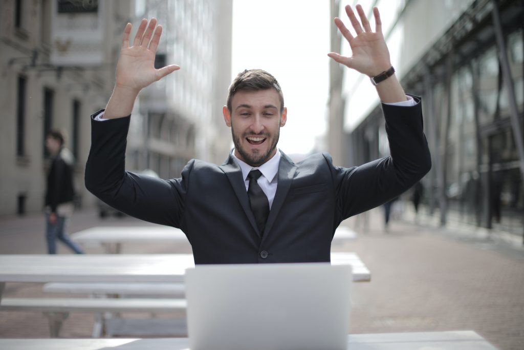 Orang yang mengangkat kedua tangannya ke udara dengan tanda seru sambil melihat ke layar laptop