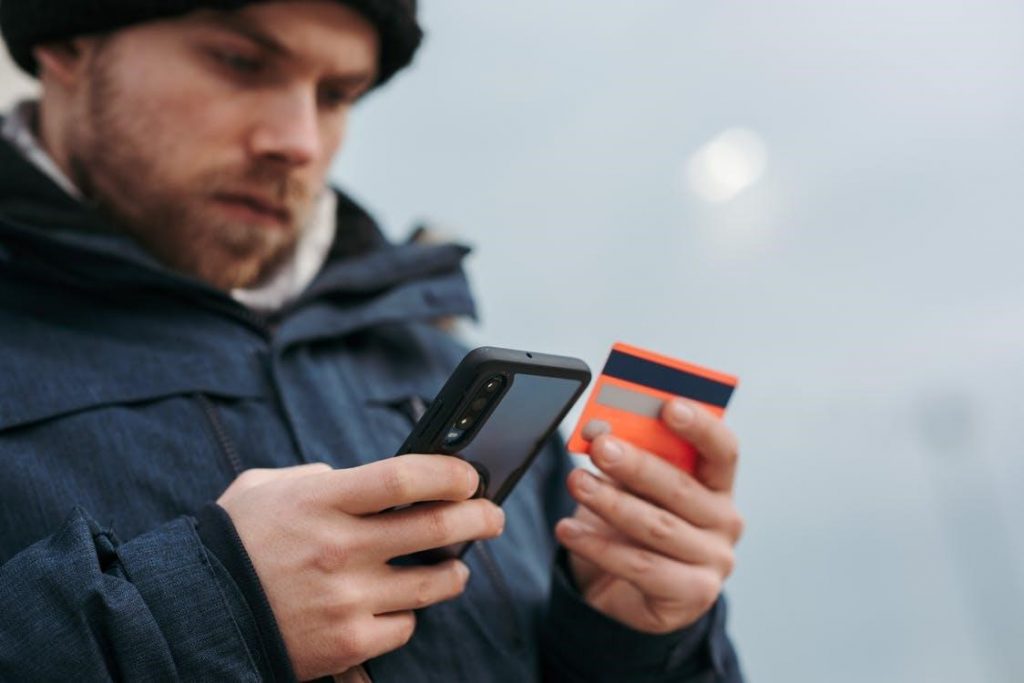 Uomo serio che paga gli acquisti online utilizzando lo smartphone per strada