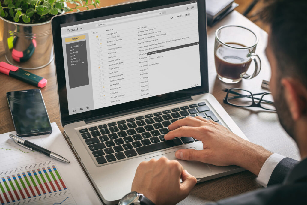 Hombre trabajando con una laptop. Lista de correos electrónicos en la pantalla, fondo de oficina