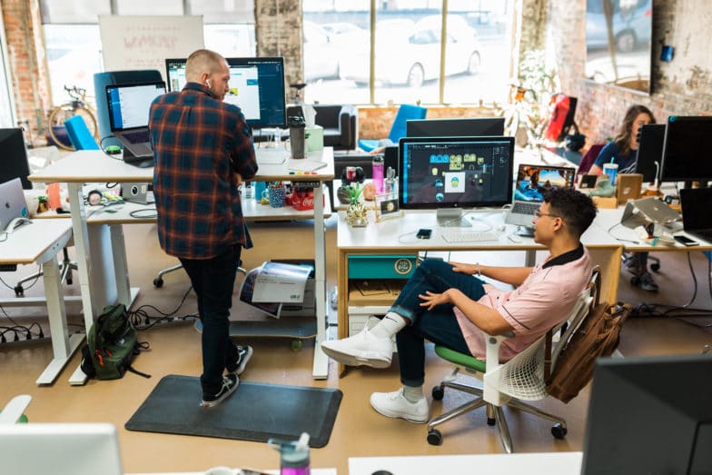 Deux personnes parlent ensemble à des bureaux adjacents, l'une est debout, l'autre est assise