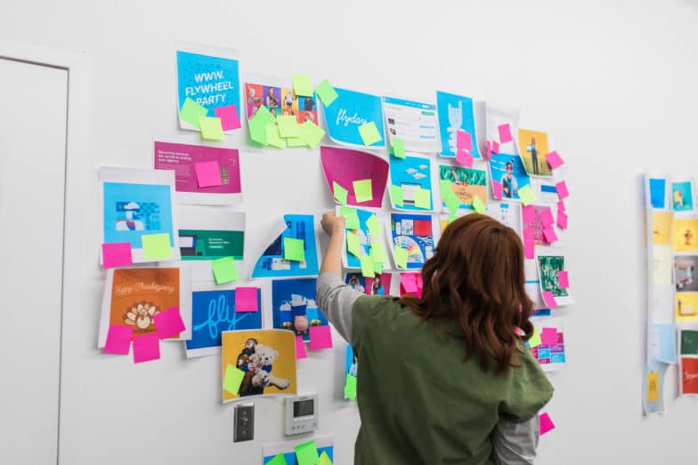 una mujer reorganiza hojas de papel con diferentes diseños en una pared blanca