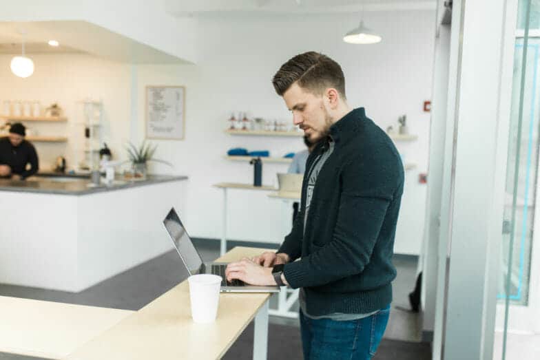 Ein Mann steht an einem Tisch in einem Café und tippt auf einem Laptop