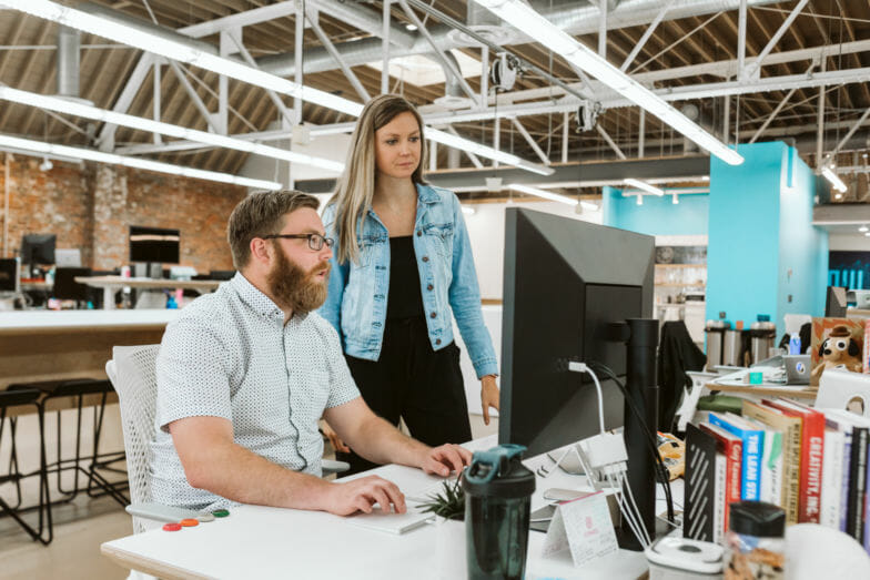 ein mann und eine frau schauen in einem offenen büro auf einen desktop-bildschirm