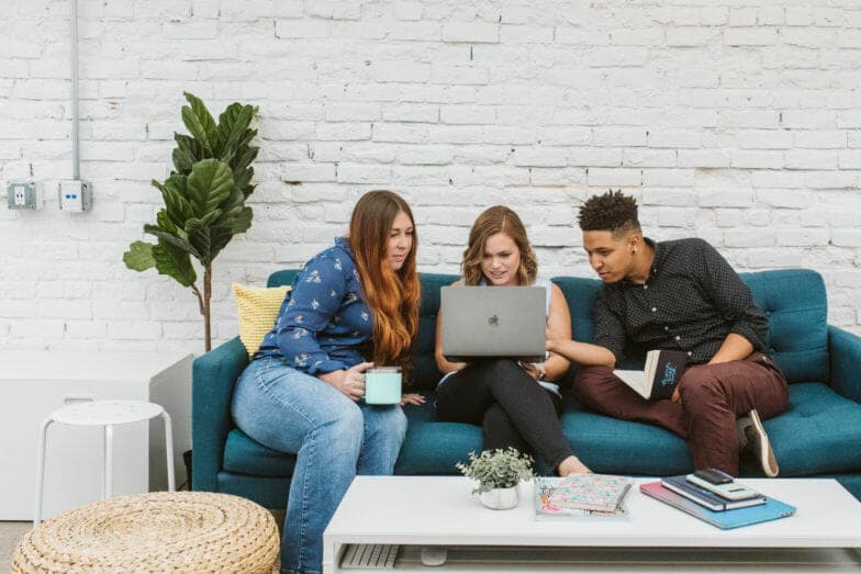 Drei Personen arbeiten gemeinsam an einem Projekt, während sie auf einer blauen Couch sitzen