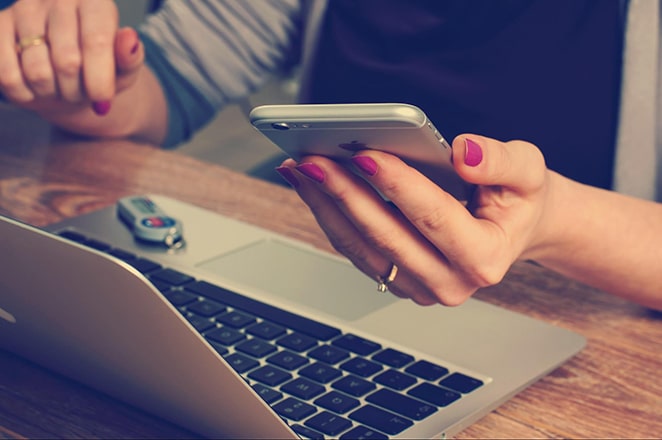 frau, die iphone und macbook-laptop auf schreibtisch hält