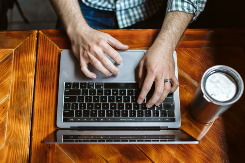 Fotografía cenital de un hombre escribiendo en una computadora portátil en un escritorio de madera