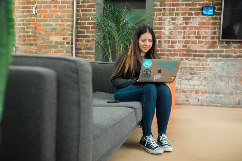 una mujer sentada en un sofá gris trabaja en una laptop