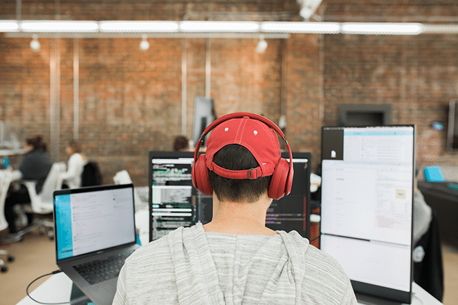 persona que trabaja en código con múltiples escritorios y pantallas en sombrero rojo