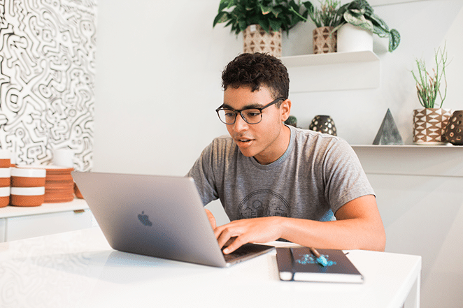 person im hellen weißen raum auf laptop und mit notizbuch in der nähe