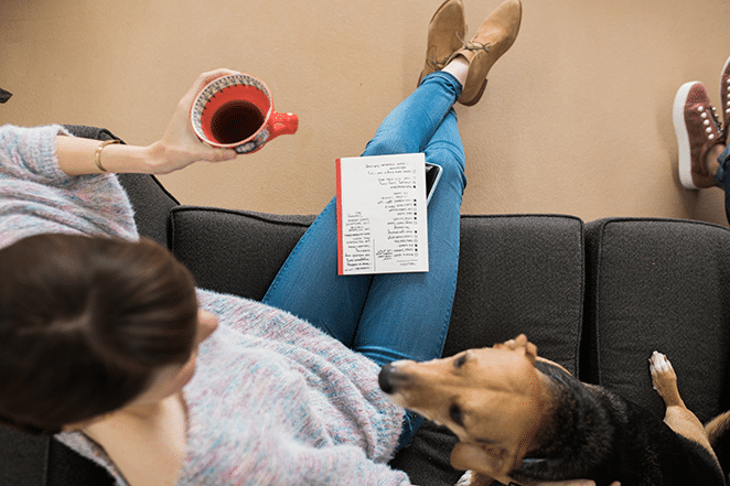 wanita dan anjing di sofa dengan teh di tangan dan buku catatan dengan daftar metrik konten untuk sukses