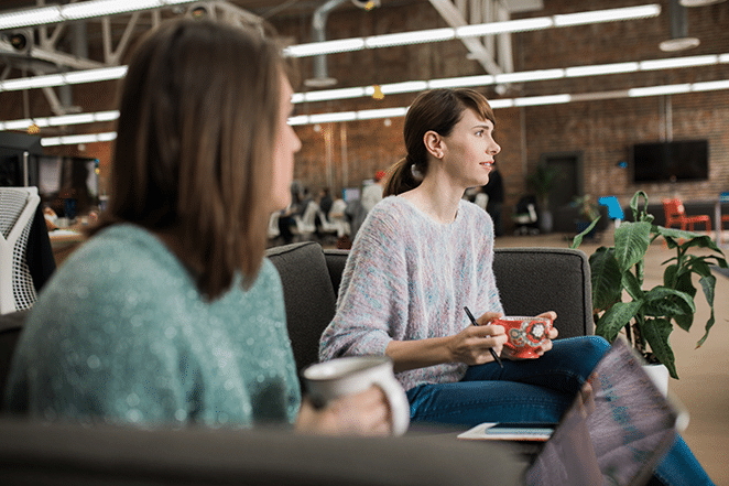 las mujeres sentadas en el sofá hablan y sostienen una taza de té colorida mientras otra mira