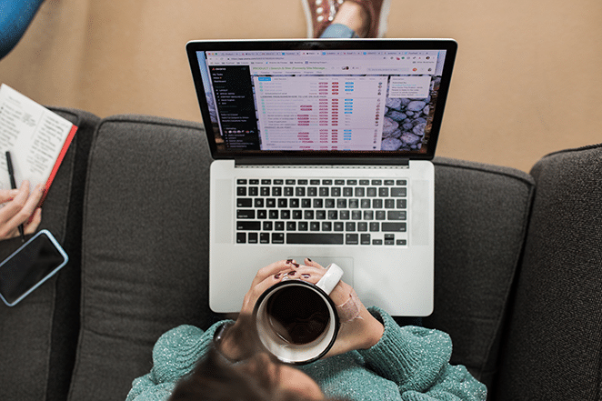 mujer con café en la mano y métricas de contenido en la computadora portátil