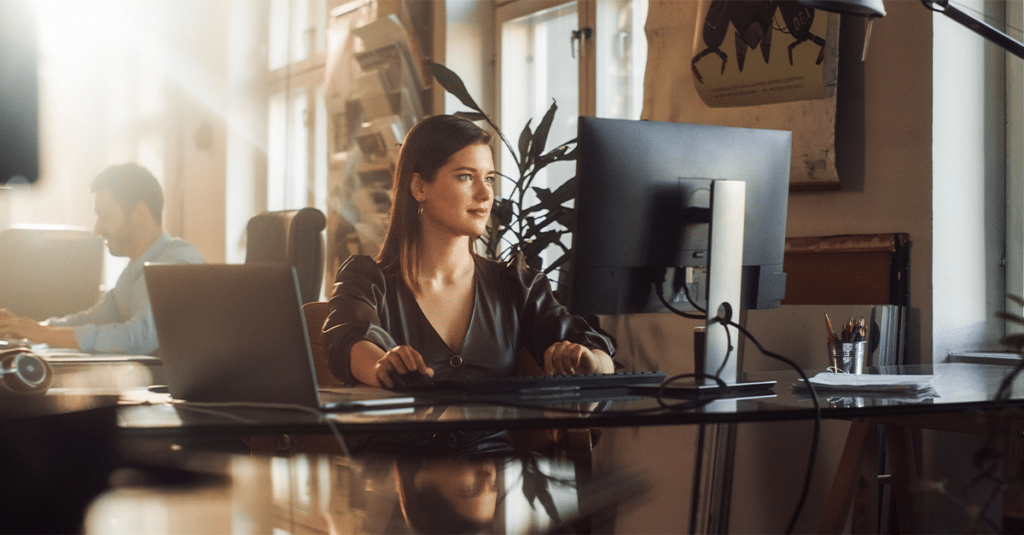 Femme travaillant à l'ordinateur dans un bureau, homme travaillant à l'ordinateur en arrière-plan