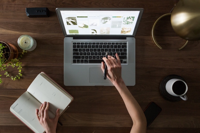 una mano fa clic su un laptop mentre l'altra tiene aperto un taccuino