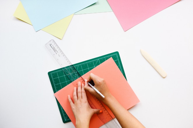 les mains utilisent une règle et un couteau x-acto pour couper du papier de construction de couleur pêche