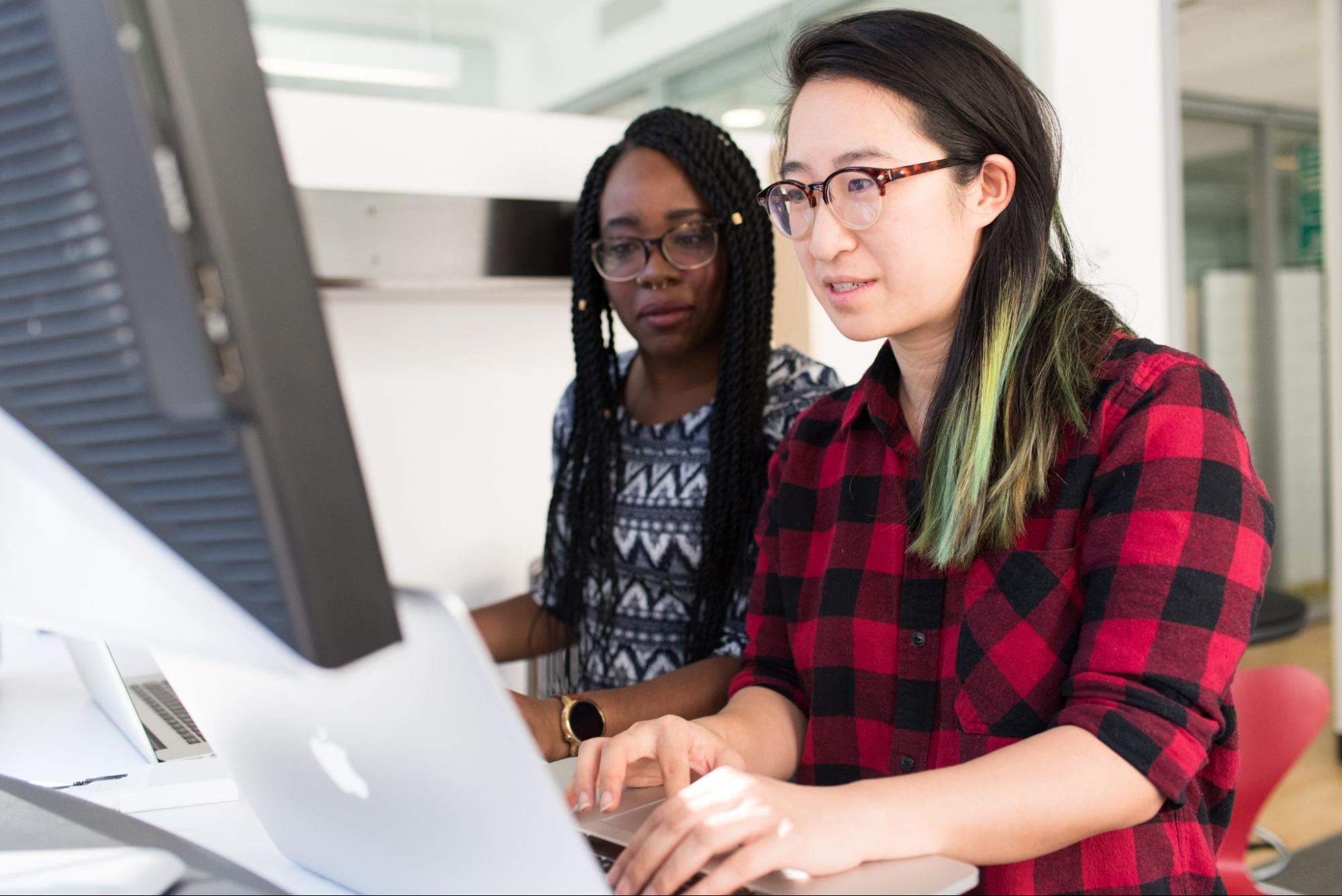 dos mujeres desarrolladoras trabajando en una computadora de escritorio