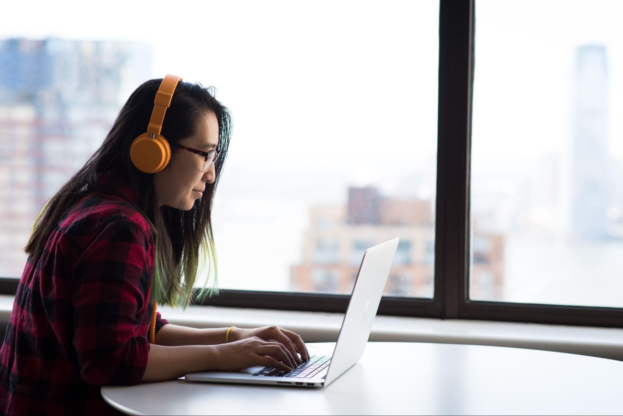 mujer trabajando en una laptop, usando audífonos