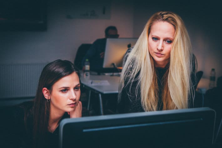 Zwei Frauen schauen in einem dunklen Raum auf einen Computerbildschirm