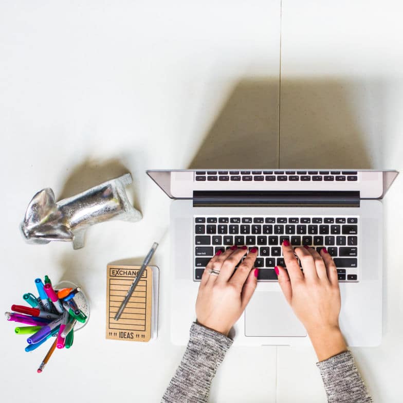 Fotografía cenital de un diseñador web con las uñas pintadas de rojo escribiendo en una computadora portátil