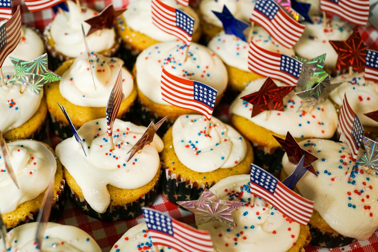 Weiße Cupcakes mit weißem Zuckerguss und roten, weißen und blauen Streuseln, aus denen jeweils kleine amerikanische Flaggen und Sterne herausragen.