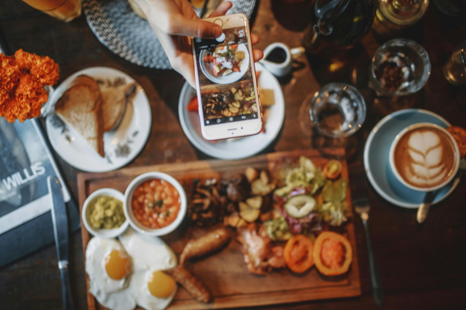 スマートフォンを使用して素朴なカフェで朝食の食べ物とコーヒーの写真を撮る人。