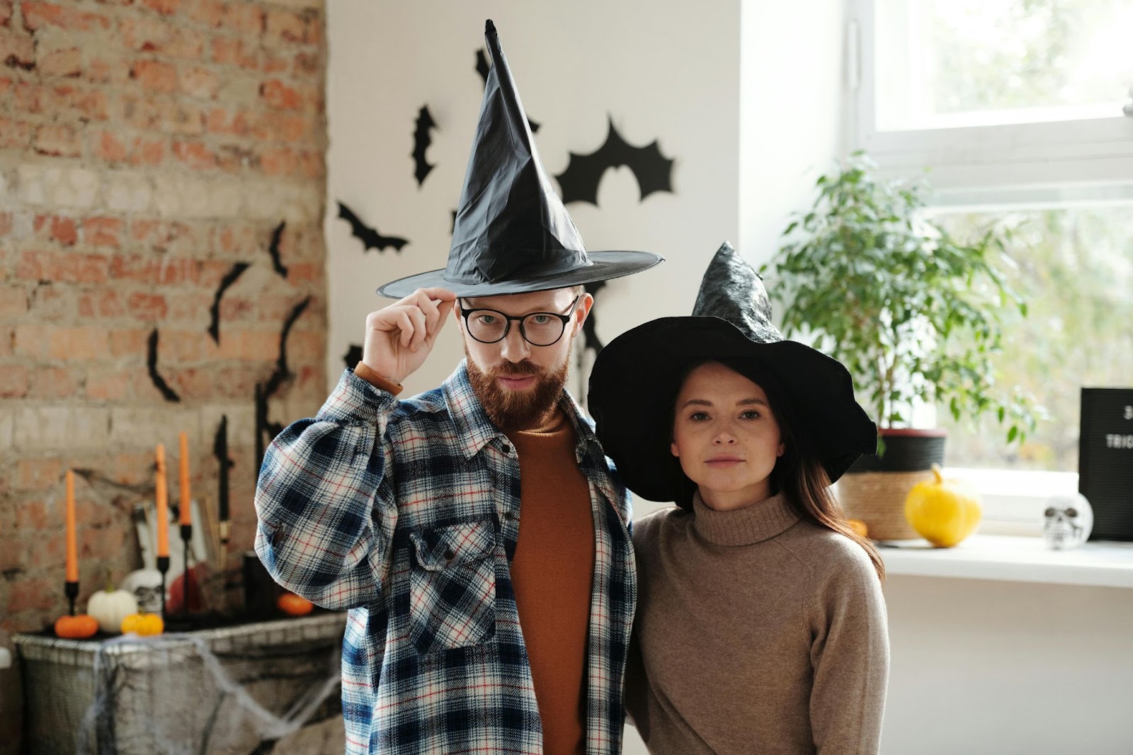 Un uomo e una donna che indossano cappelli da strega in un ufficio rustico decorato con altri elementi stagionali come candele, zucche e teschi.